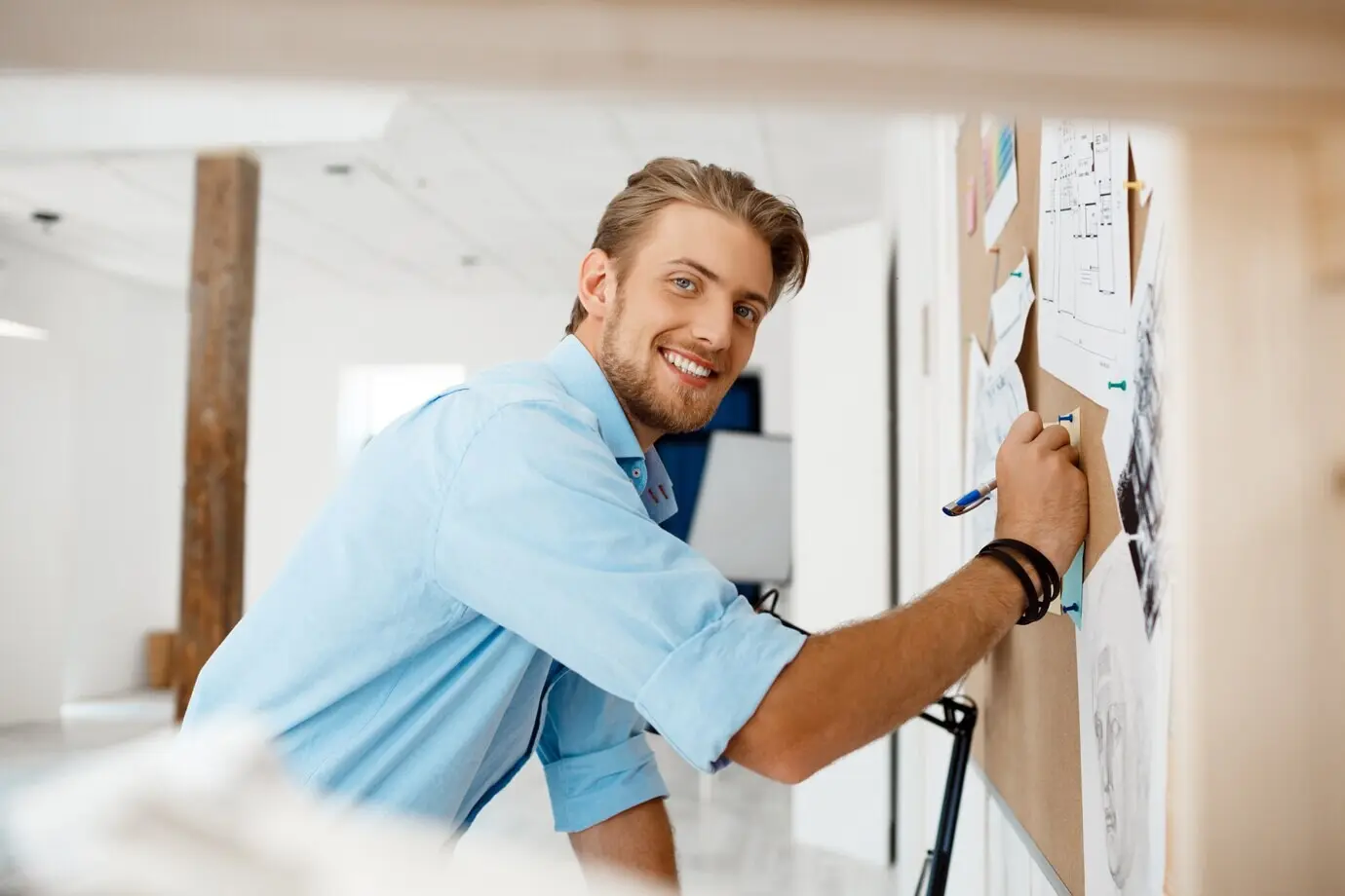 A young, handsome businessman writes on the paper pinned to a corkboard.