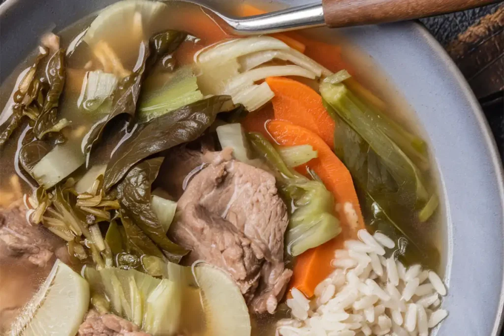 A bowl of Sinigang with pork, vegetables, and tamarind